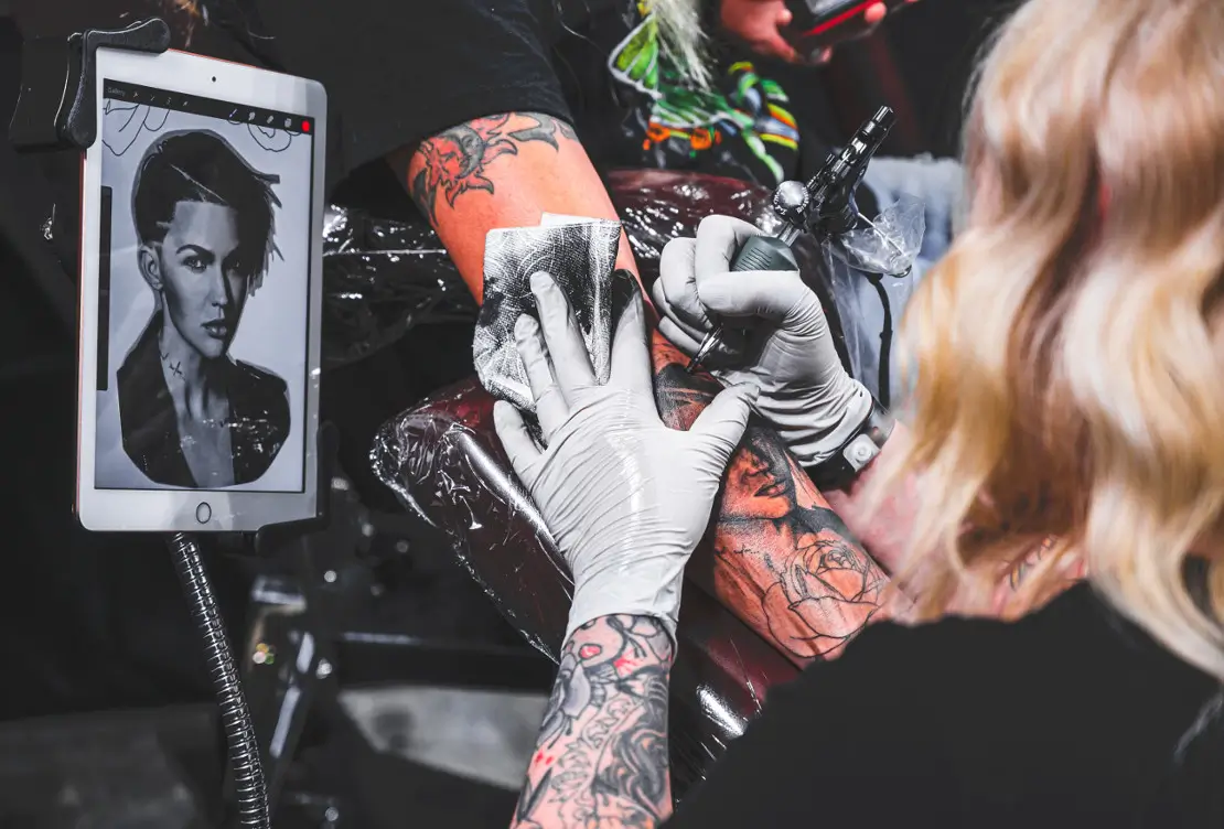 Tattoo Studio artist inking an arm with ipad showing work photograph