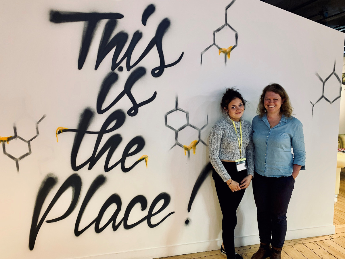 a girl, Cherry Passmore, and a woman, Sophie Walker, standing infront of a sign saying this is the place